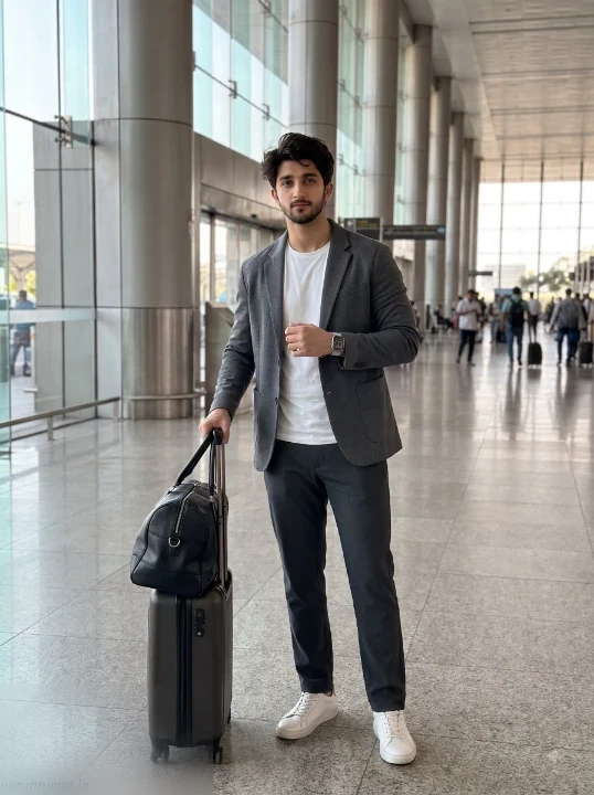 Man in charcoal relaxed blazer and white T-shirt standing beside suitcase in spacious international airport departure hall using ChatGPT travel prompt for boys