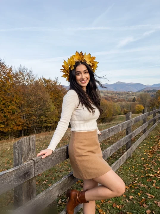 Girl wearing ivory ribbed top and camel mini skirt with autumn leaf wreath, standing beside wooden countryside fence, fall photo prompt for girls
