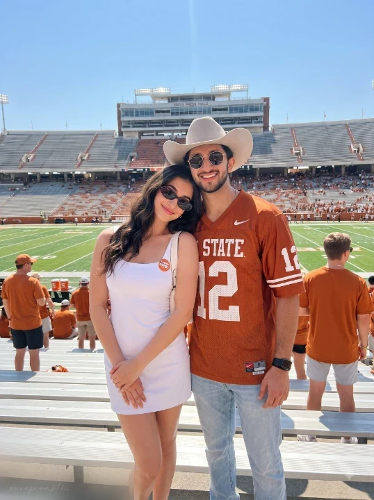 Gemini couple football photo prompt woman in white dress and man in burnt orange jersey with cowboy hat on college stadium bleachers